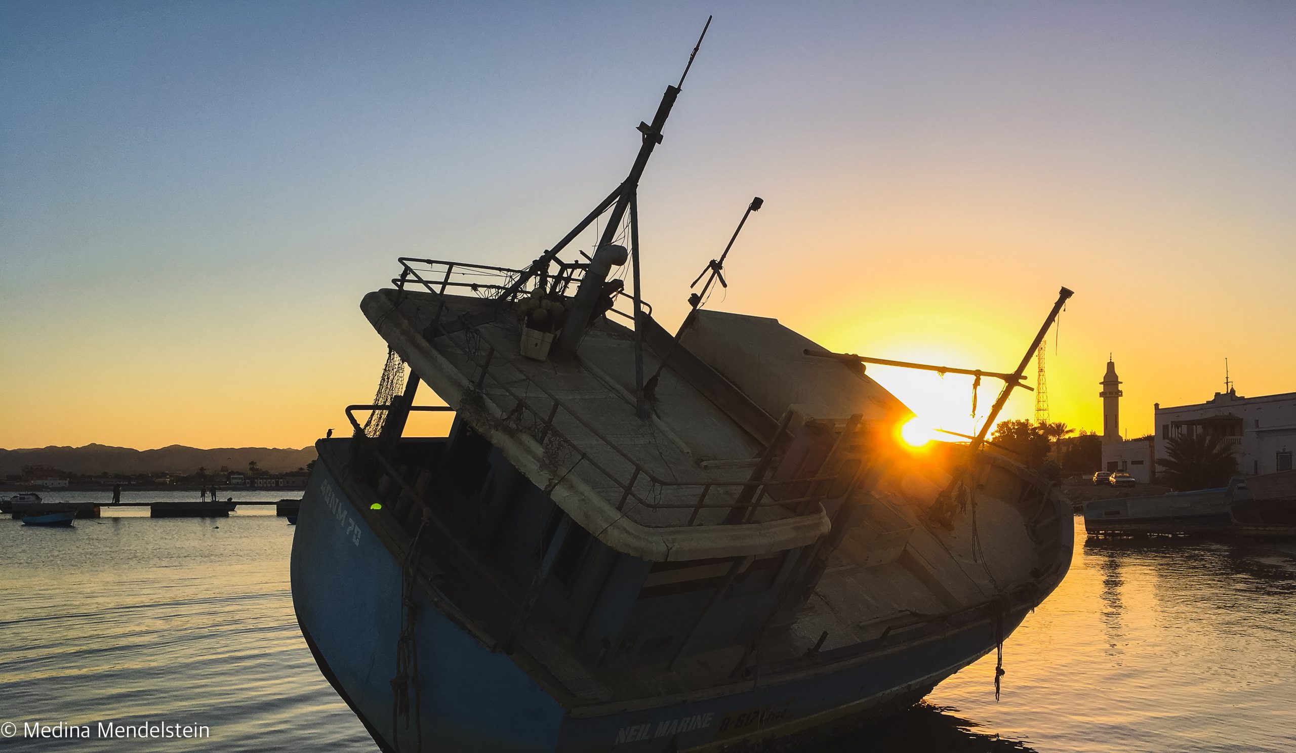 Fotografie aus: al-Quasai in Ägypten, Afrika: Ein altes Boot liegt im Hafen. Die Sonne vom Sonnenuntergang steht genau zwischen Bug und Steuerhaus.