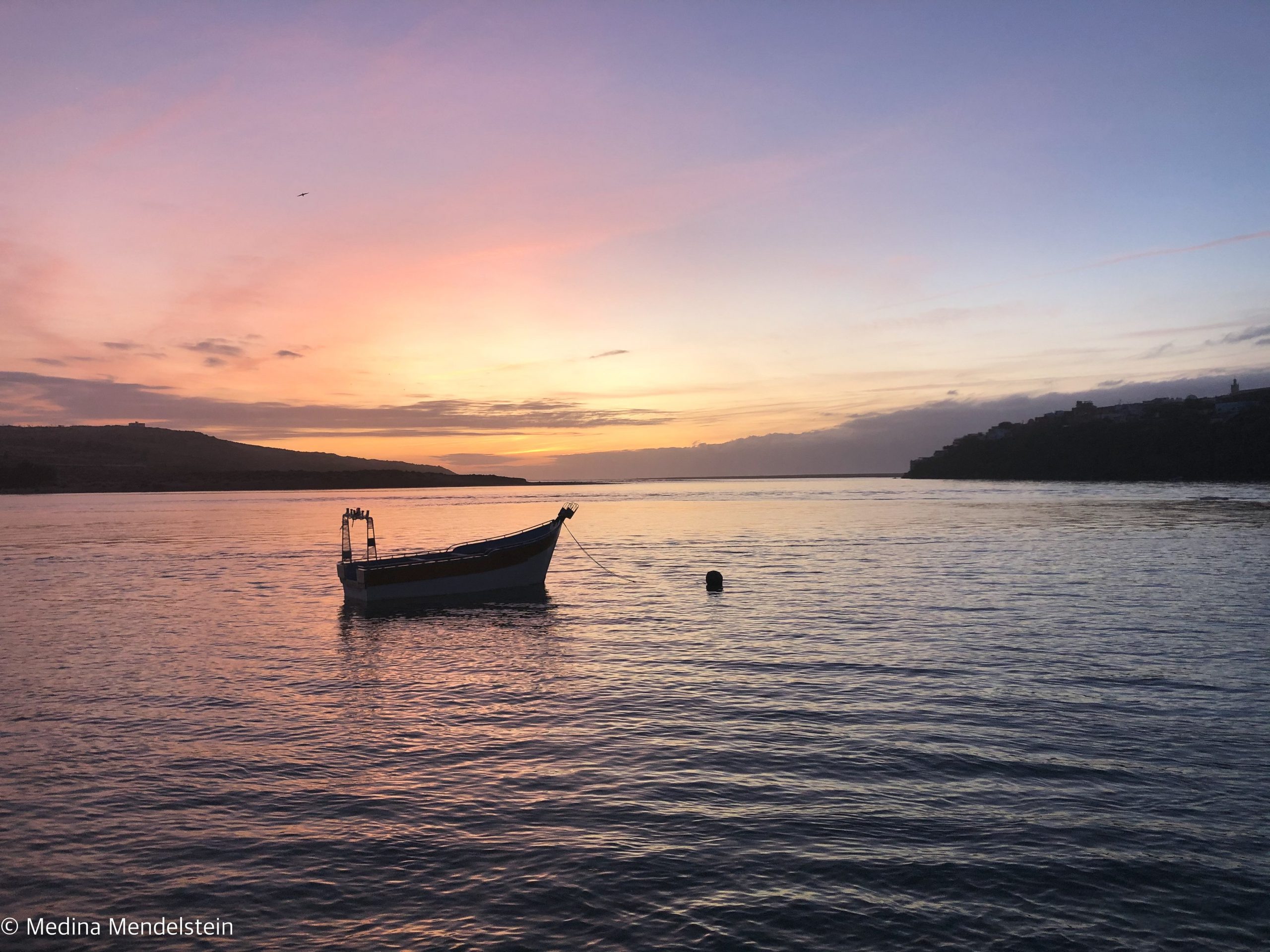 Fotografie aus: Moulay Bousselham in Marokko, Afrika: Sonnenuntergang am Wasser, im Vordergrund ist die Silhouette eines Fischerboots zu sehen.