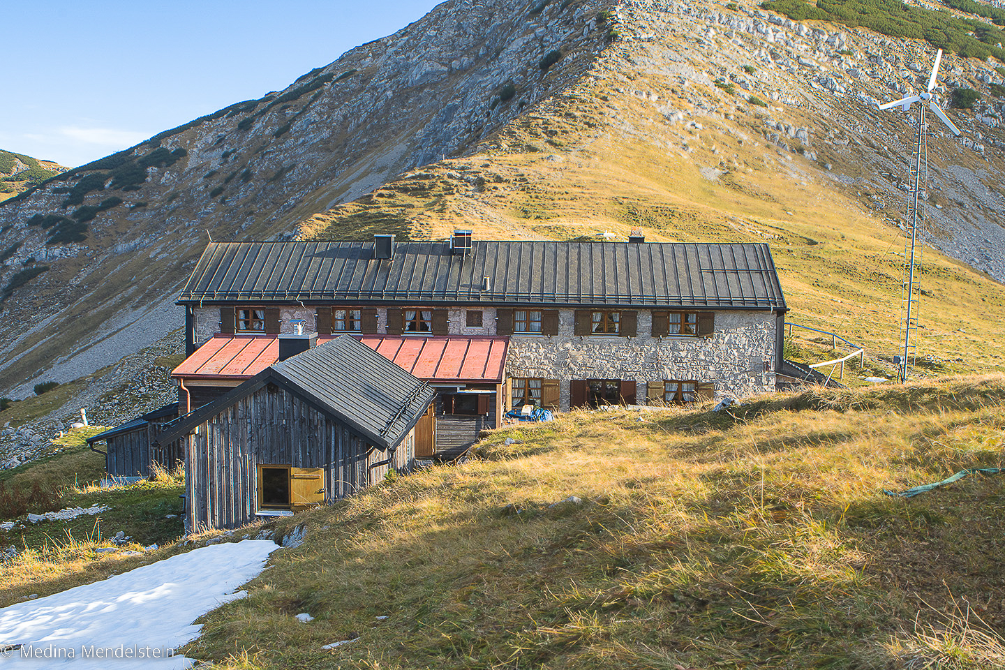 Die Weilheimer Hütte in den Alpen von vorne. Vor der Alm liegt ein bisschen Schnee. Direkt dahinter ist der Krottenkopf zu sehen.