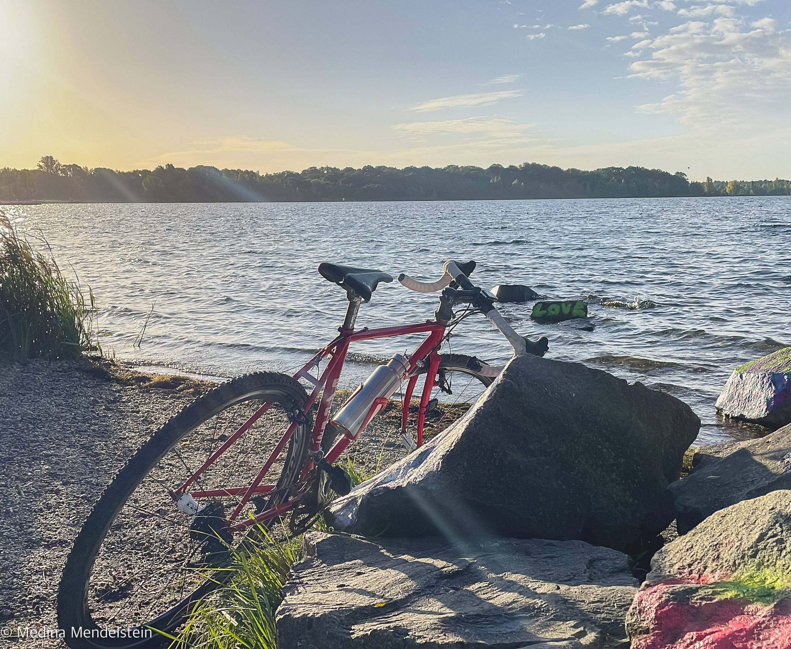 Rennrad bei einer Radreise lehnt an Steinen. Es steht auf einem Steinstrand am Wasser.